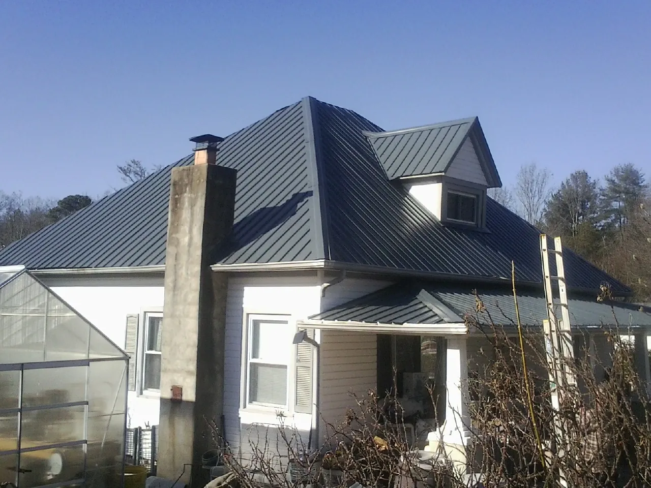 Dark blue standing seam metal roof on a white farmhouse with dormer — Slate & Tile Roof Repair by Roofing Brothers in Humphrey