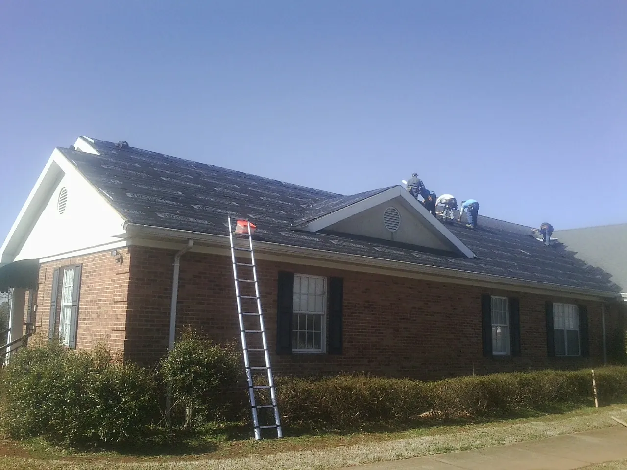 Crew tearing shingles off a brick ranch roof with a ladder set — Emergency Roof Repair work by our crew in Humphrey