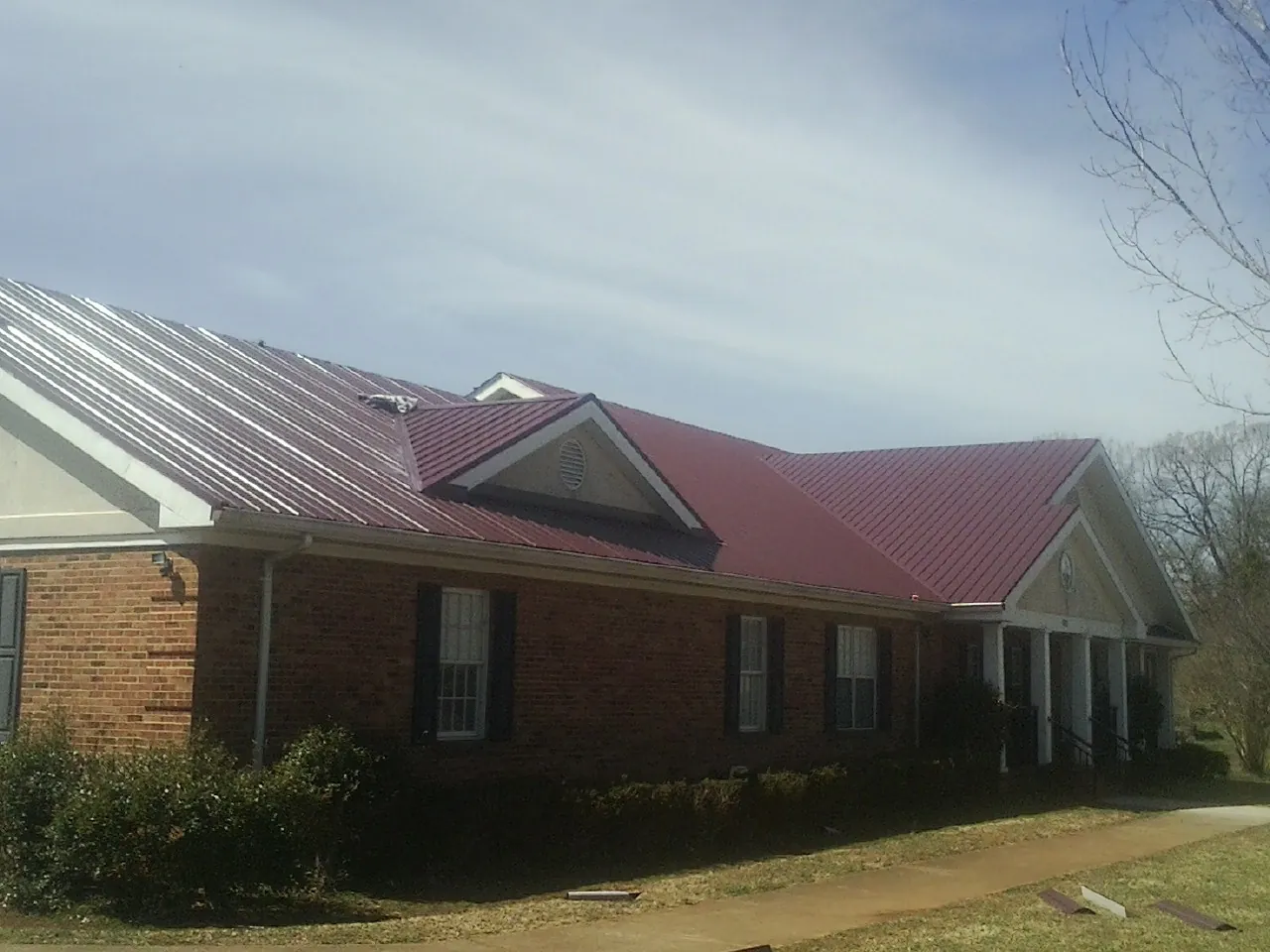 Red metal roof with gabled entries on a long brick building, from a Hail Damage Roof Repair job in Humphrey