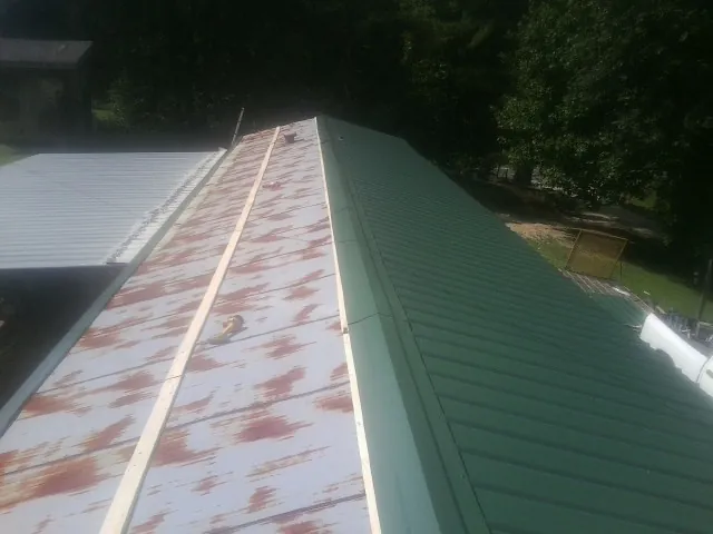 Old rusted panels beside newly installed green metal roofing — Wind Damage Roof Repair by Roofing Brothers in Humphrey