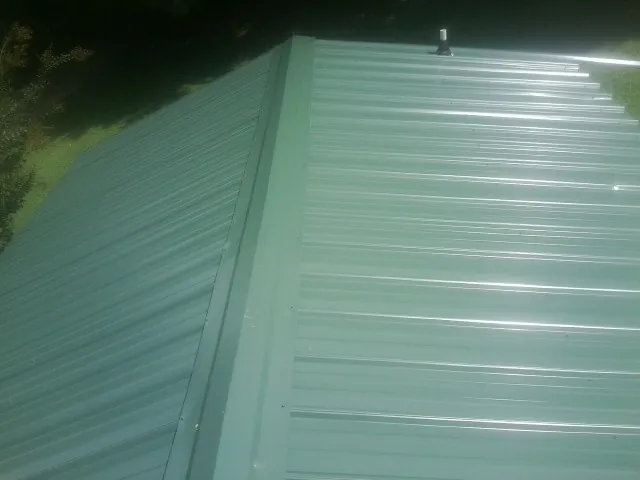 New green metal panels meeting at the ridge of a roof — Flat Roof Repair work by our crew in Humphrey