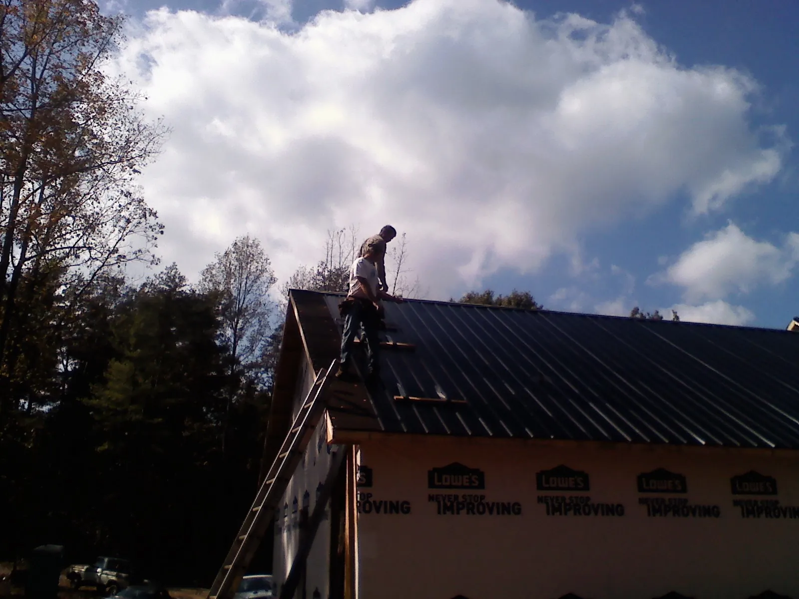 Roofer fastening dark metal panels high against a cloudy sky, from a Roof Inspection job in Humphrey