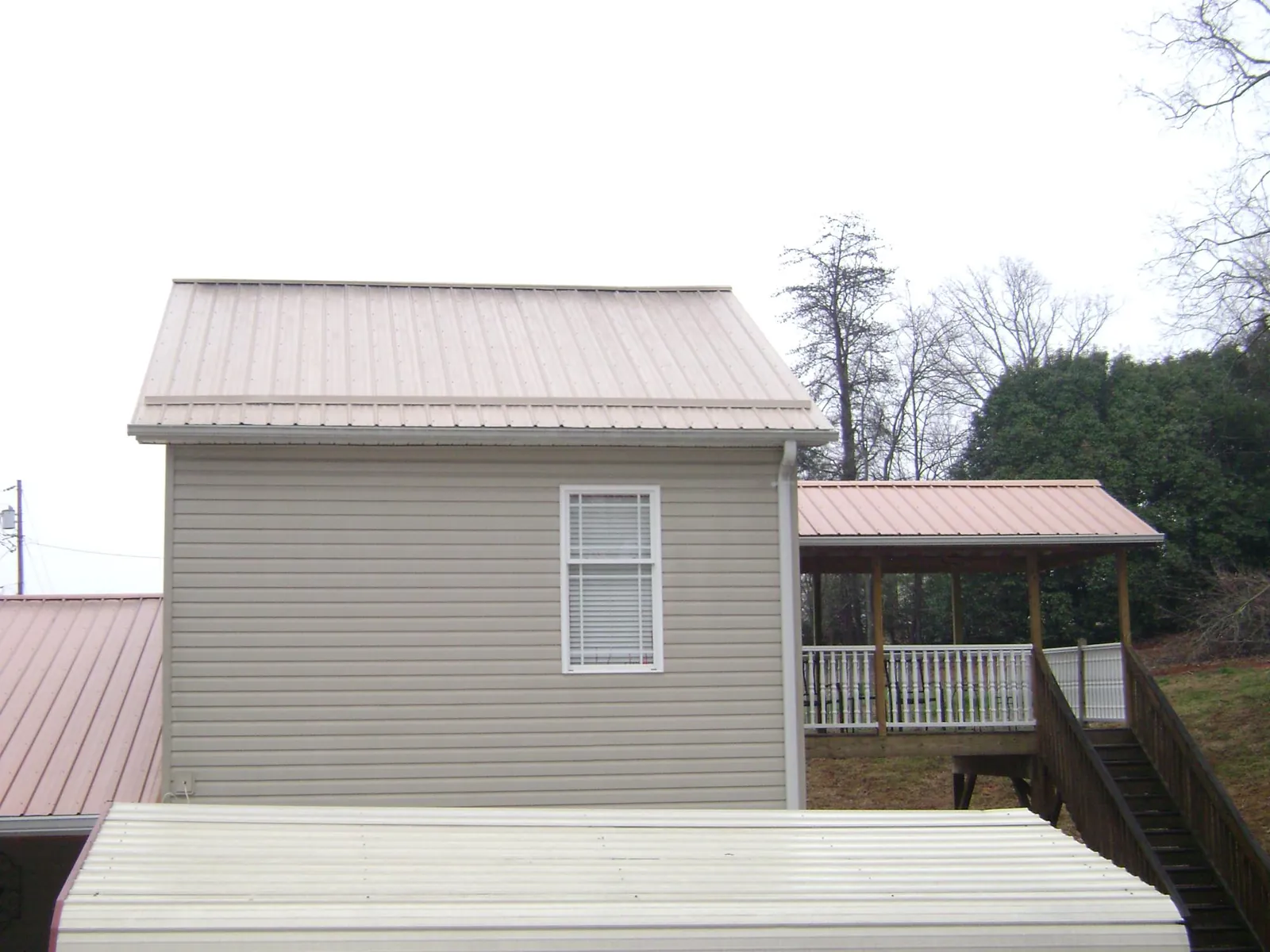Tan metal roofs on a two story addition and attached porch, from a Roof Replacement job in Humphrey