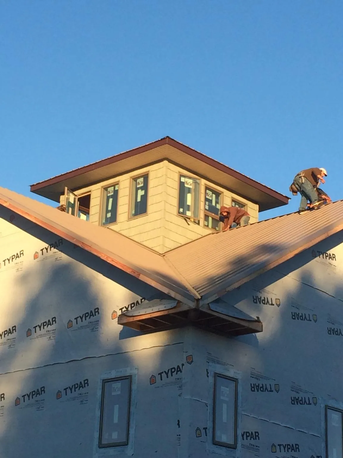 Roofers working around a rooftop cupola on a new metal roof at sunset — Roof Waterproofing in Humphrey by Roofing Brothers